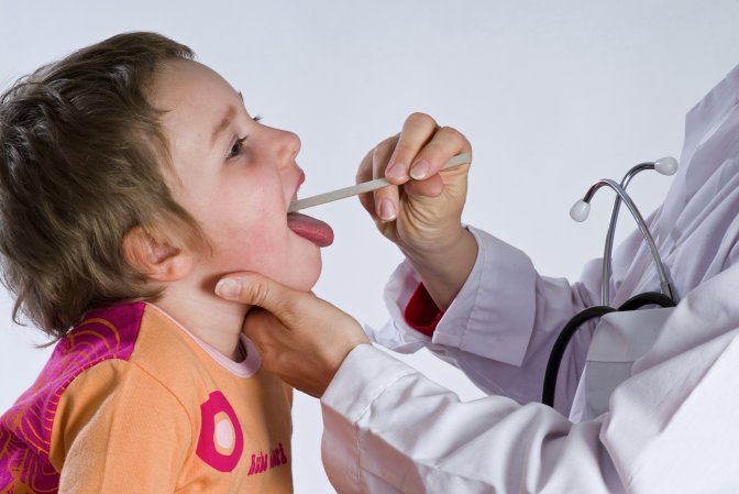 a doctor uses a tongue depressor to look down a child's throat