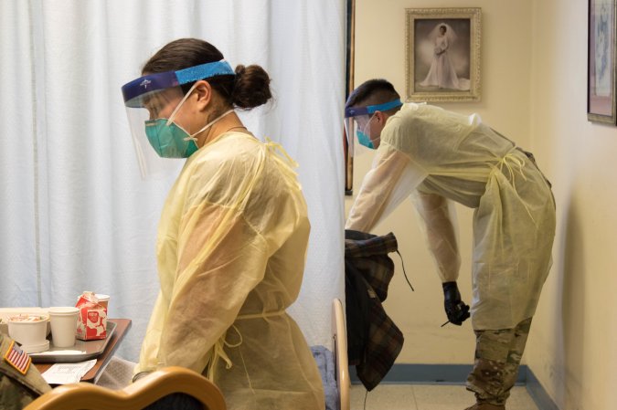 two people in protective gear stand by hospital beds