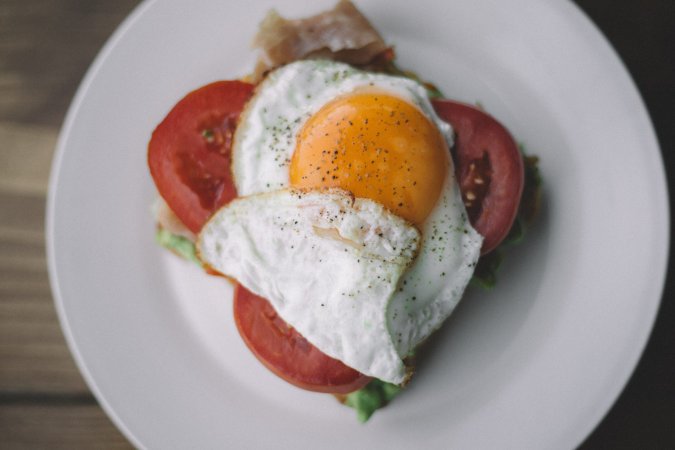 a fried egg on top of tomatoes on a white plate