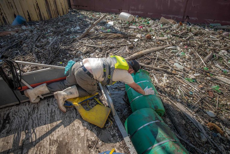 a boat captain tries to pull a plastic barrel from a debris island