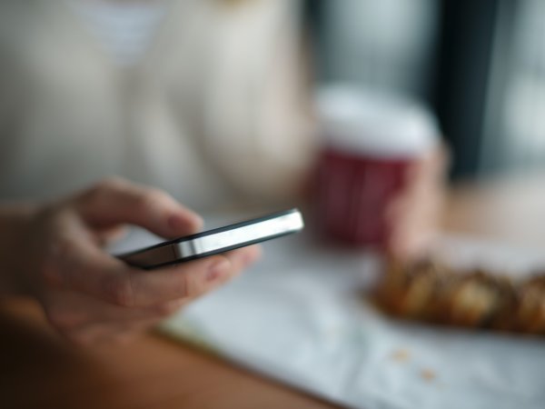 A person holding their phone while drinking coffee, possibly deleting text message attachments from their device.