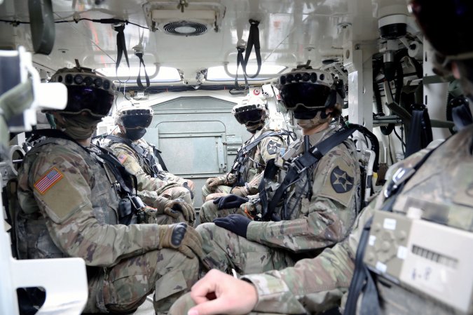 Soldiers wearing augmented reality headsets while sitting in a vehicle.