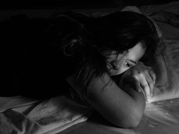 A woman lying on a bed in dim light, looking lonely.