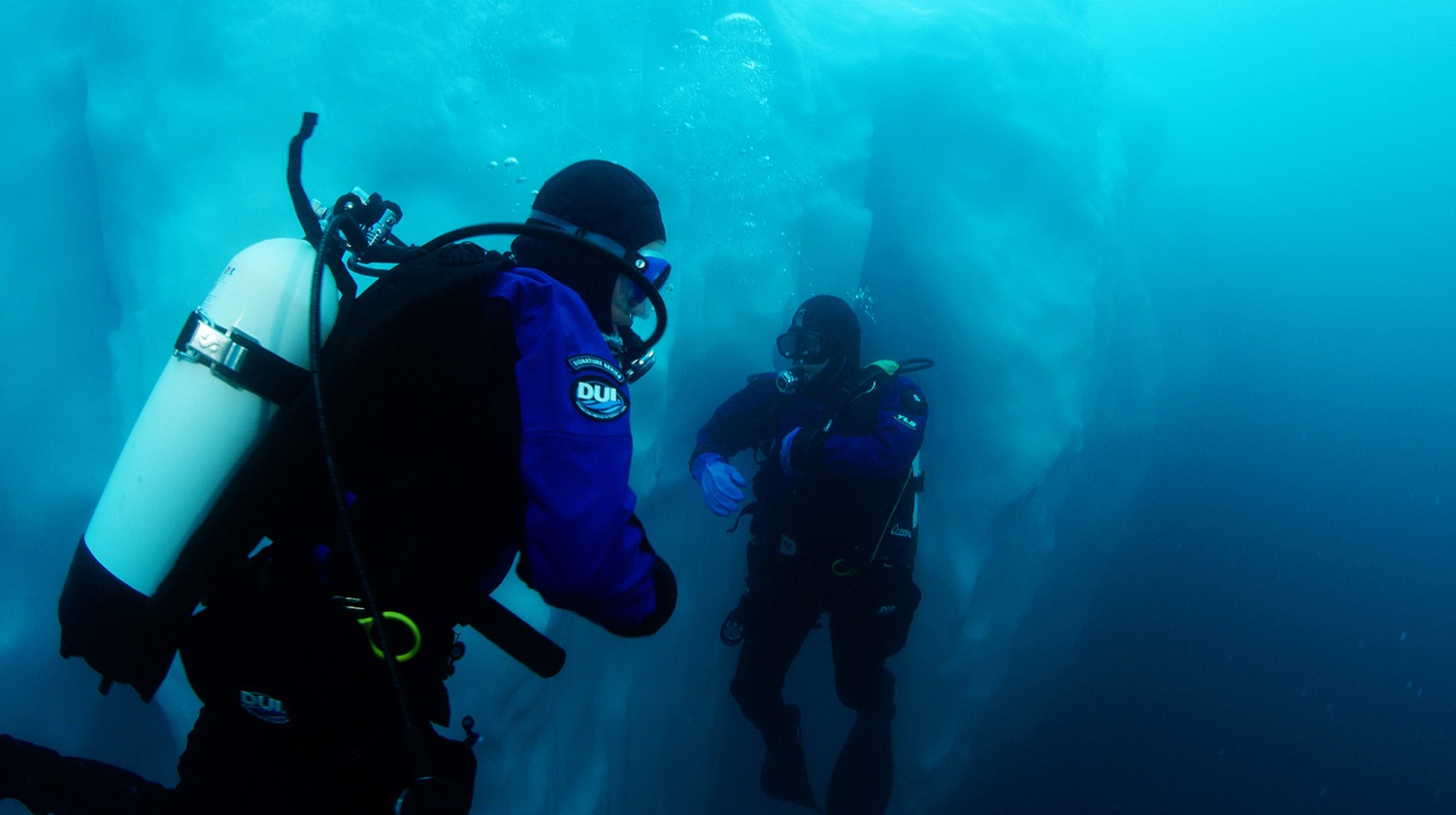 two people in scuba gear under the water near an iceburg
