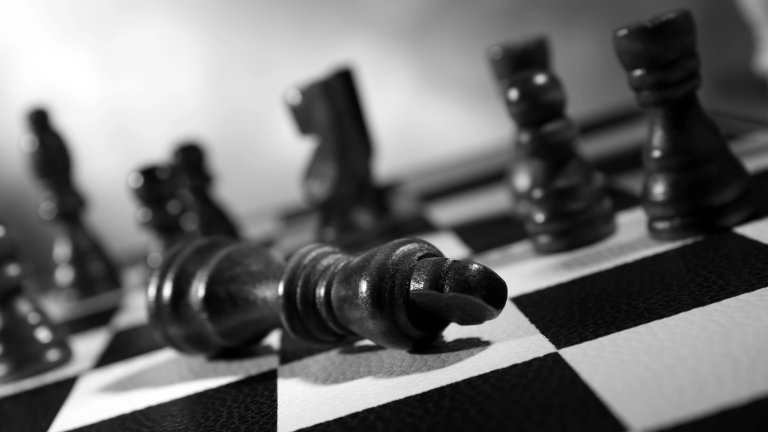 Close up of black chess pieces on chessboard with king knocked over